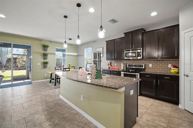 kitchen featuring pendant lighting, an island with sink, appliances with stainless steel finishes, tasteful backsplash, and dark brown cabinets