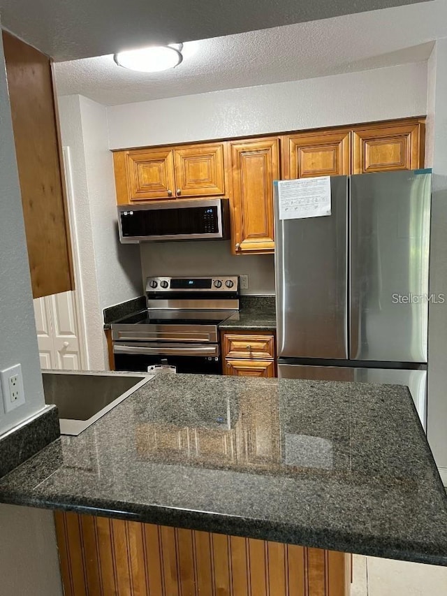 kitchen with dark stone counters, a textured ceiling, and appliances with stainless steel finishes