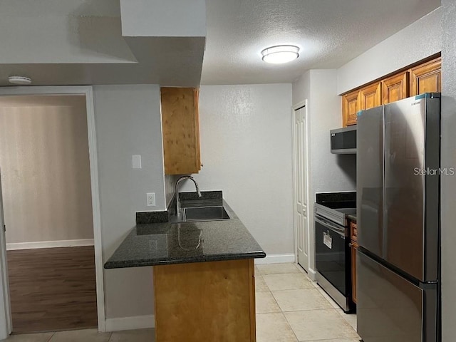 kitchen with sink, light tile patterned floors, stainless steel appliances, and dark stone counters