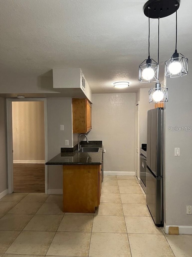 kitchen with hanging light fixtures, sink, light tile patterned floors, and stainless steel refrigerator