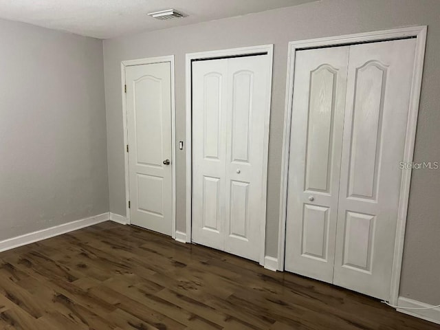 unfurnished bedroom with two closets and dark wood-type flooring