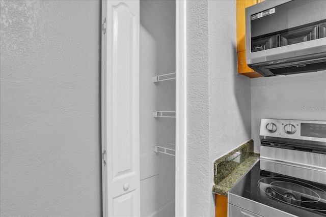 room details featuring appliances with stainless steel finishes, a textured wall, and dark countertops