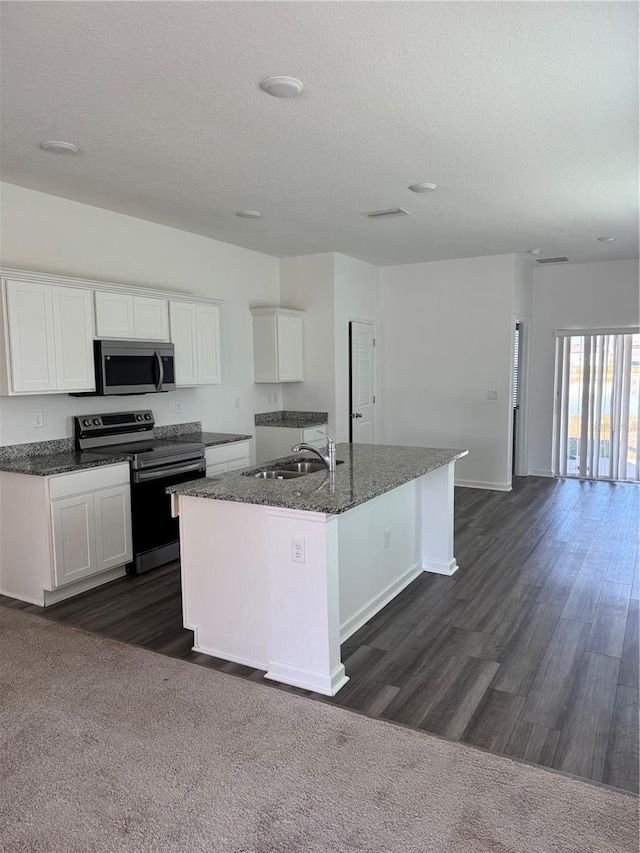 kitchen featuring white cabinetry, sink, stainless steel appliances, dark stone countertops, and an island with sink