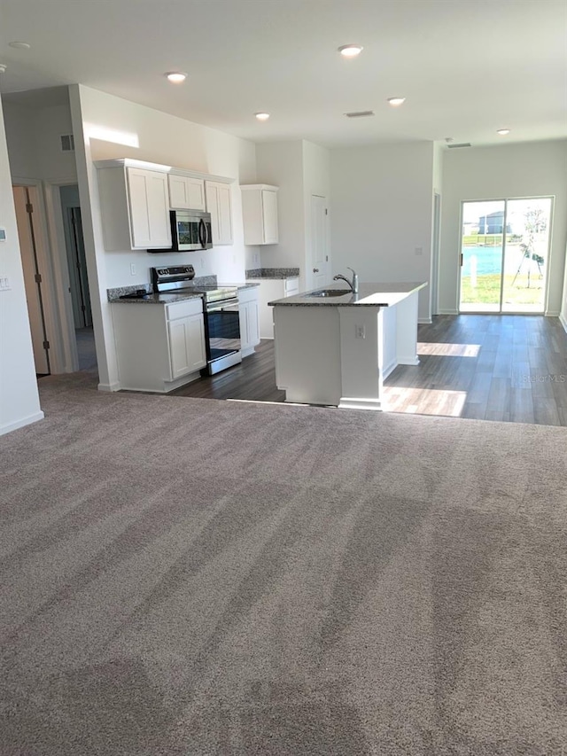 kitchen with carpet, a center island with sink, sink, white cabinetry, and stainless steel appliances