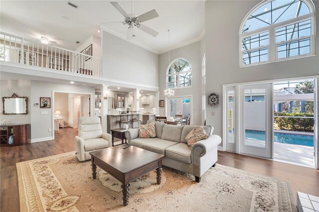 living room featuring a high ceiling, wood-type flooring, crown molding, and ceiling fan