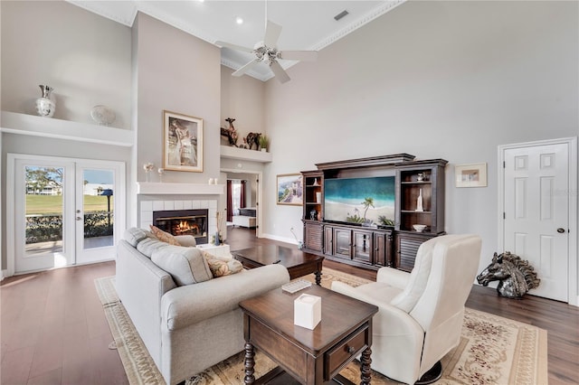 living room featuring ceiling fan, a towering ceiling, wood-type flooring, and a fireplace