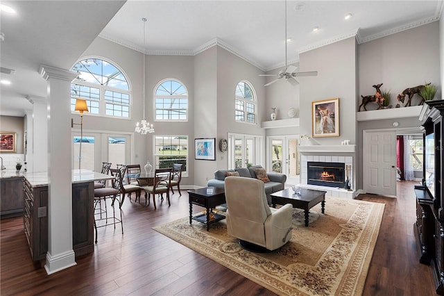 living room featuring ornate columns, a tile fireplace, dark hardwood / wood-style flooring, ornamental molding, and plenty of natural light