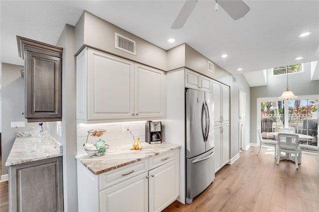 kitchen featuring pendant lighting, stainless steel refrigerator, white cabinets, decorative backsplash, and light wood-type flooring