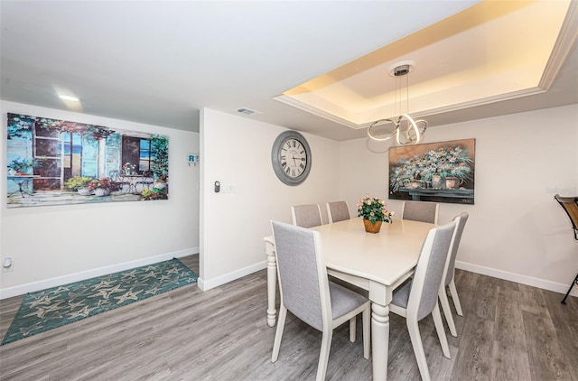 dining space with wood-type flooring, a tray ceiling, and an inviting chandelier