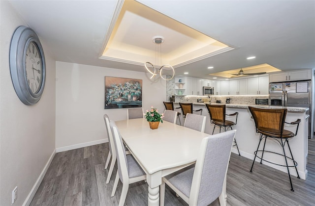 dining room with light hardwood / wood-style floors, a raised ceiling, and ceiling fan