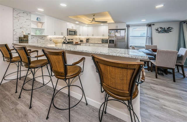 kitchen with kitchen peninsula, light hardwood / wood-style floors, a breakfast bar area, white cabinets, and appliances with stainless steel finishes