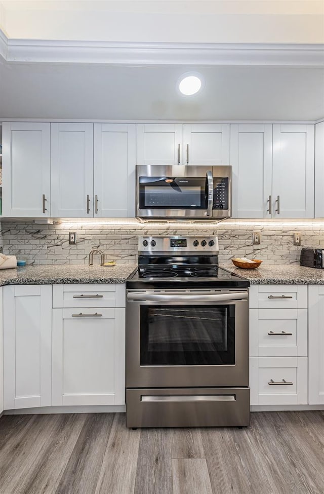 kitchen with decorative backsplash, light stone counters, stainless steel appliances, light hardwood / wood-style flooring, and white cabinetry