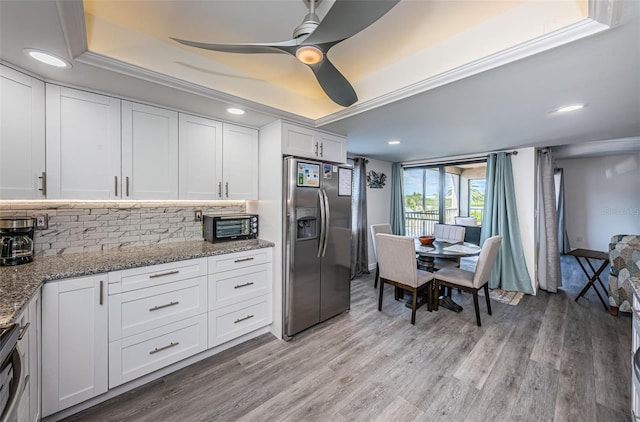 kitchen with a raised ceiling, ceiling fan, stainless steel fridge, light wood-type flooring, and white cabinetry