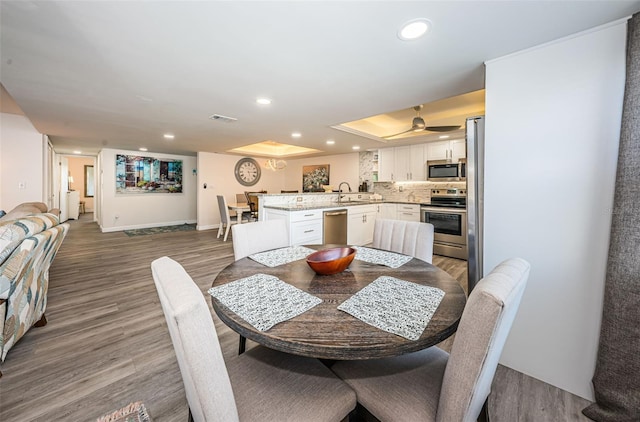 dining room with hardwood / wood-style floors, a raised ceiling, ceiling fan, and sink