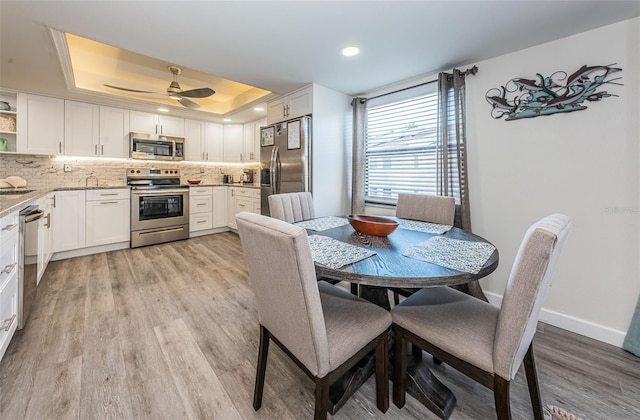 dining area featuring light wood-type flooring, a raised ceiling, and ceiling fan