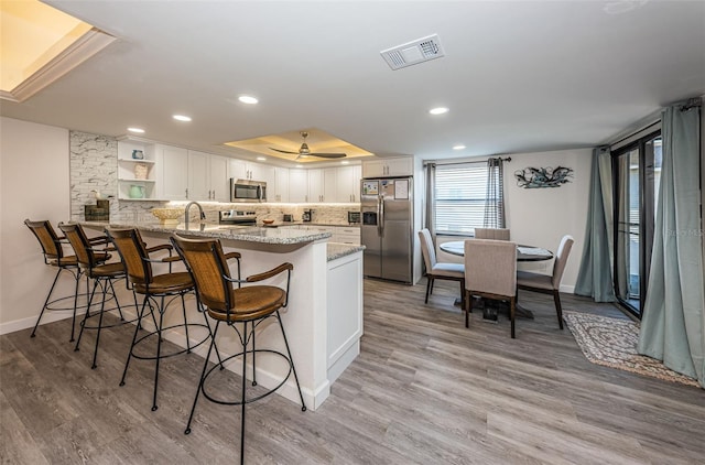 kitchen with kitchen peninsula, light hardwood / wood-style flooring, appliances with stainless steel finishes, light stone counters, and white cabinetry