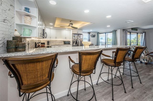 kitchen featuring white cabinets, light stone countertops, a kitchen bar, kitchen peninsula, and stainless steel appliances