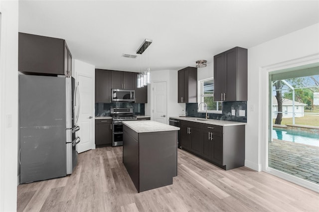 kitchen featuring decorative light fixtures, a kitchen island, light hardwood / wood-style floors, and appliances with stainless steel finishes