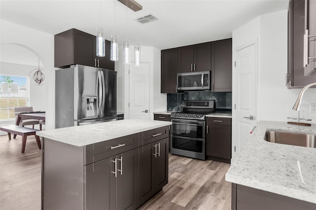 kitchen featuring sink, stainless steel appliances, light hardwood / wood-style flooring, pendant lighting, and a kitchen island