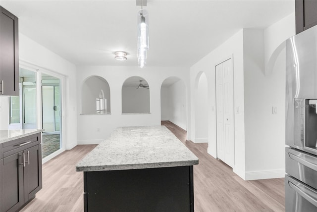 kitchen with a center island, light stone counters, light hardwood / wood-style flooring, stainless steel fridge, and decorative light fixtures