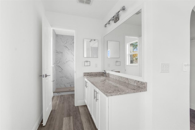 bathroom with hardwood / wood-style floors, vanity, and tiled shower