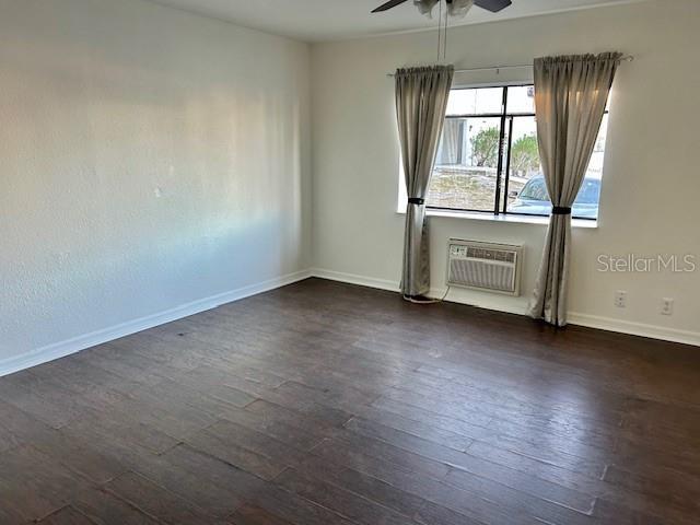 empty room featuring ceiling fan, dark hardwood / wood-style floors, and a wall unit AC