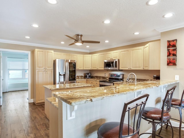 kitchen with kitchen peninsula, appliances with stainless steel finishes, a kitchen bar, dark hardwood / wood-style flooring, and ceiling fan