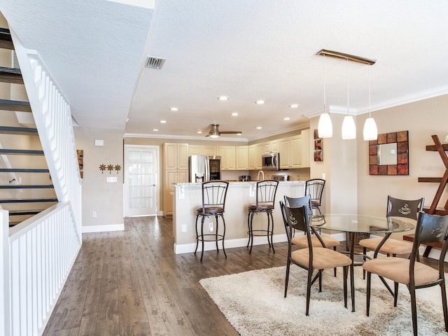 dining area with ceiling fan, dark hardwood / wood-style flooring, ornamental molding, and a textured ceiling