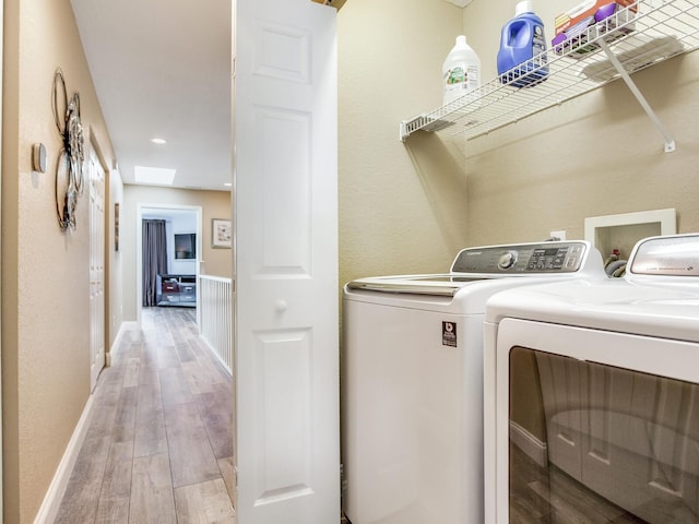 laundry room featuring light wood-type flooring, independent washer and dryer, and a skylight