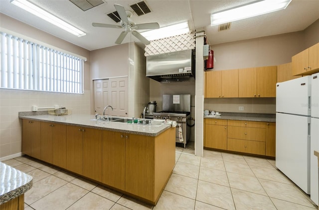 kitchen featuring light tile patterned floors, high end stove, ceiling fan, wall chimney range hood, and white refrigerator