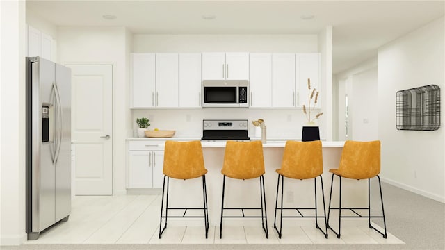 kitchen with a kitchen island with sink, white cabinetry, a breakfast bar area, and appliances with stainless steel finishes