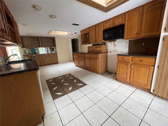 kitchen featuring light tile patterned floors, a skylight, tasteful backsplash, and sink