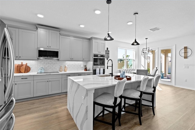 kitchen featuring light stone countertops, appliances with stainless steel finishes, a breakfast bar, a kitchen island with sink, and hanging light fixtures