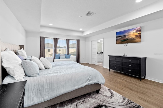 bedroom with a tray ceiling, connected bathroom, and hardwood / wood-style flooring