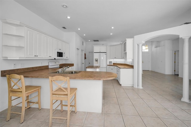 kitchen with kitchen peninsula, a kitchen breakfast bar, white appliances, sink, and white cabinetry