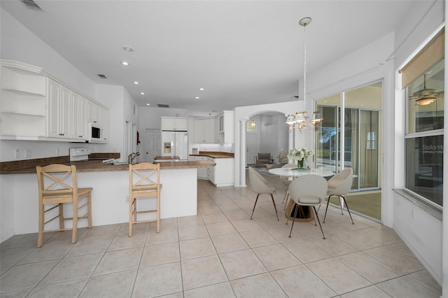 kitchen featuring light tile patterned flooring, kitchen peninsula, white appliances, a breakfast bar area, and white cabinets