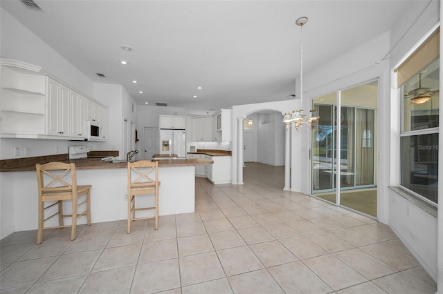 kitchen with white appliances, kitchen peninsula, light tile patterned flooring, white cabinetry, and a breakfast bar area