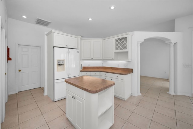 kitchen featuring a kitchen island, white cabinets, white refrigerator with ice dispenser, decorative columns, and light tile patterned floors