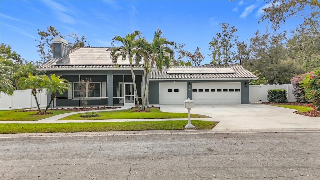 view of front of property with a garage, a front yard, a sunroom, and solar panels