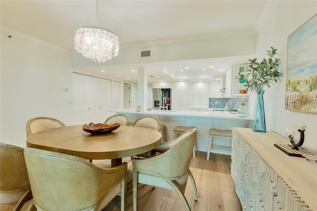 dining space with ornamental molding, light hardwood / wood-style flooring, and an inviting chandelier