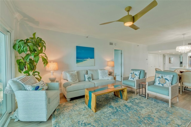 living room featuring ceiling fan with notable chandelier, light wood-type flooring, and ornamental molding