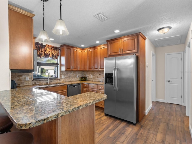 kitchen with sink, appliances with stainless steel finishes, kitchen peninsula, pendant lighting, and dark wood-type flooring