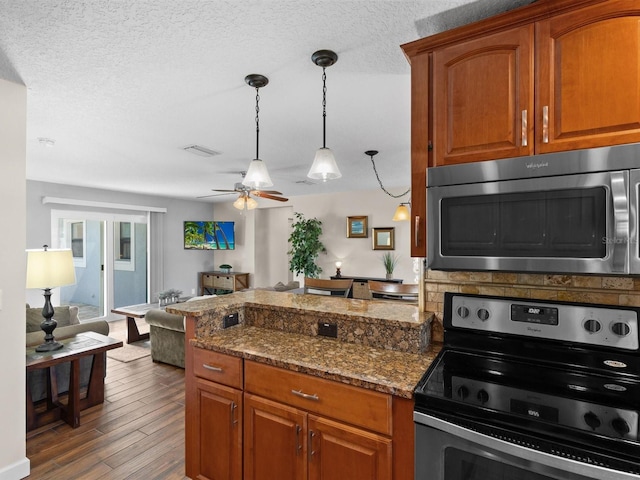 kitchen with appliances with stainless steel finishes, dark stone counters, dark wood-type flooring, ceiling fan, and a textured ceiling