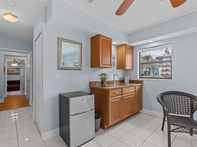 kitchen featuring sink, a textured ceiling, light tile patterned flooring, dark stone counters, and stainless steel fridge