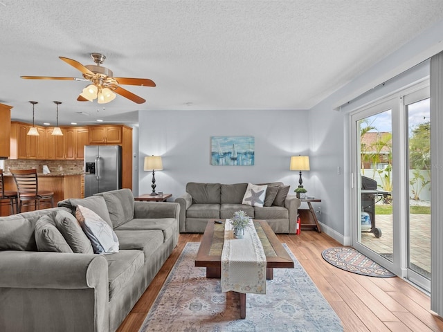 living room featuring ceiling fan, light hardwood / wood-style floors, and a textured ceiling