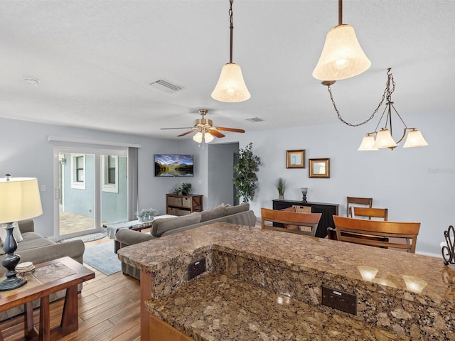 kitchen with decorative light fixtures, stone counters, ceiling fan with notable chandelier, and hardwood / wood-style flooring