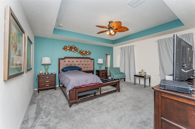 bedroom featuring a textured ceiling, light colored carpet, a raised ceiling, and ceiling fan