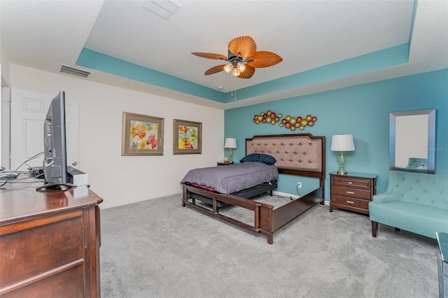 carpeted bedroom featuring a tray ceiling, ceiling fan, and a textured ceiling