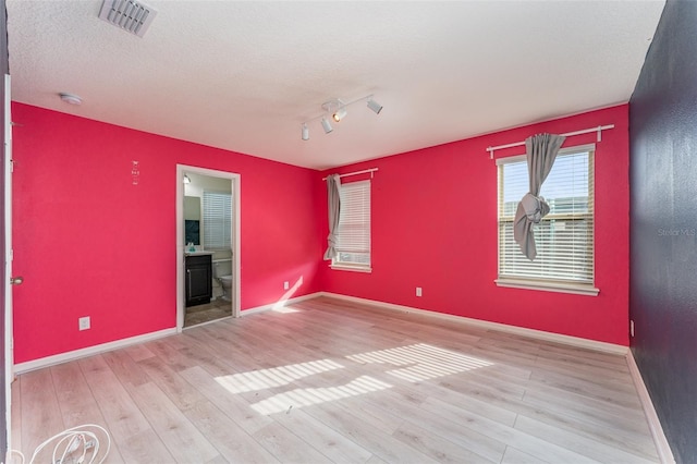 spare room with track lighting, light hardwood / wood-style floors, and a textured ceiling