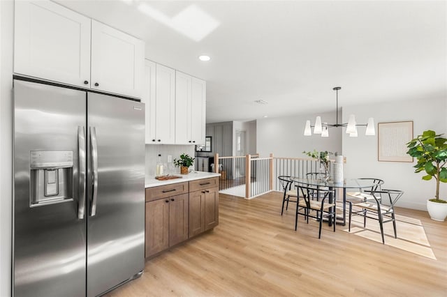 kitchen featuring backsplash, stainless steel refrigerator with ice dispenser, hanging light fixtures, a notable chandelier, and white cabinetry